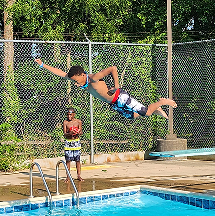 kid jumping into pool with superhero arms