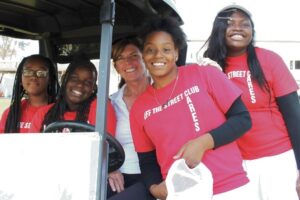 four girls and a volunteer posing on a golf cart